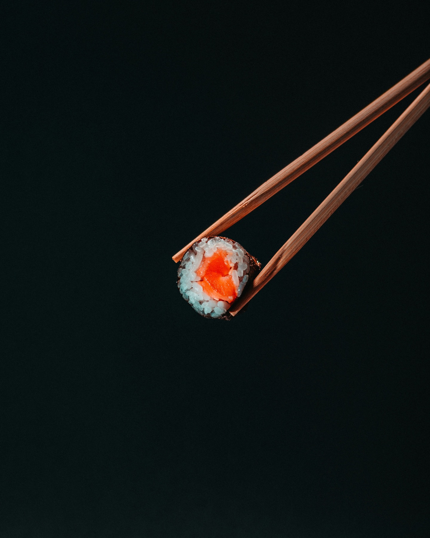 Salmon maki held by chopsticks